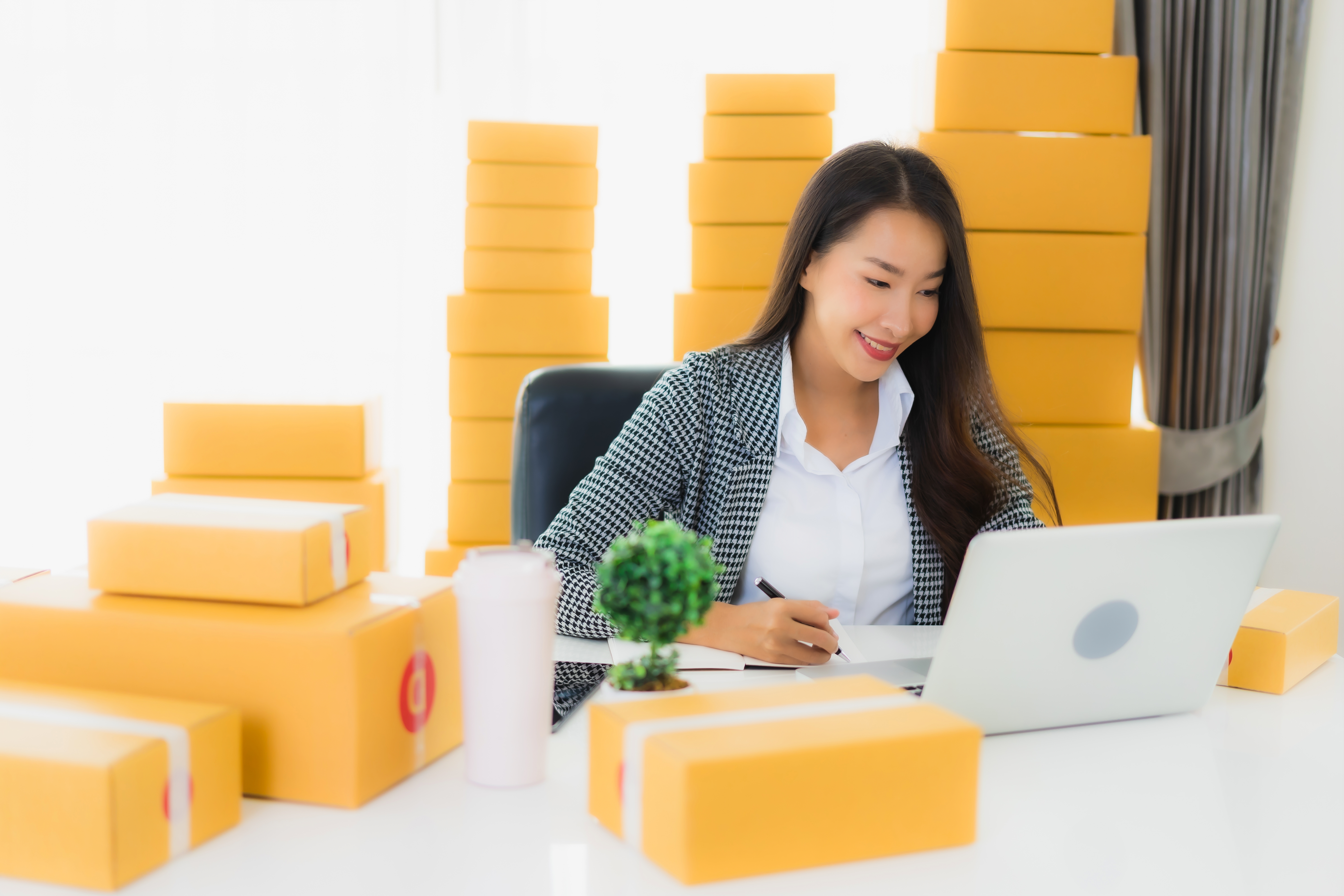 portrait-beautiful-young-asian-business-woman-work-from-home-with-laptop-mobile-phone-with-cardboard-box-ready-for-shipping